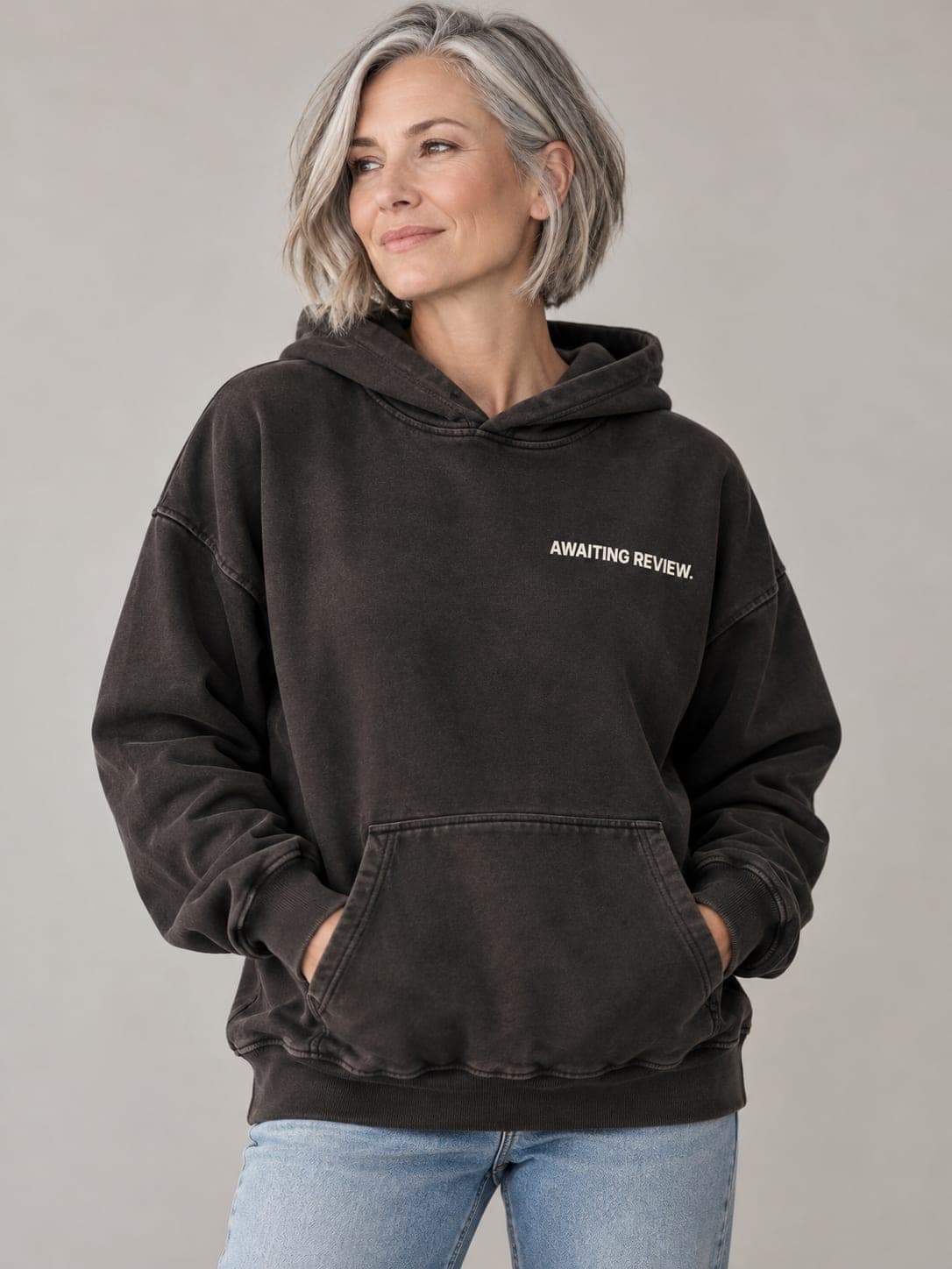 AWAITING REVIEW Hoodie in Pigment Black, worn by a model: AWAITING REVIEW. printed left chest. AI-generated mockup.