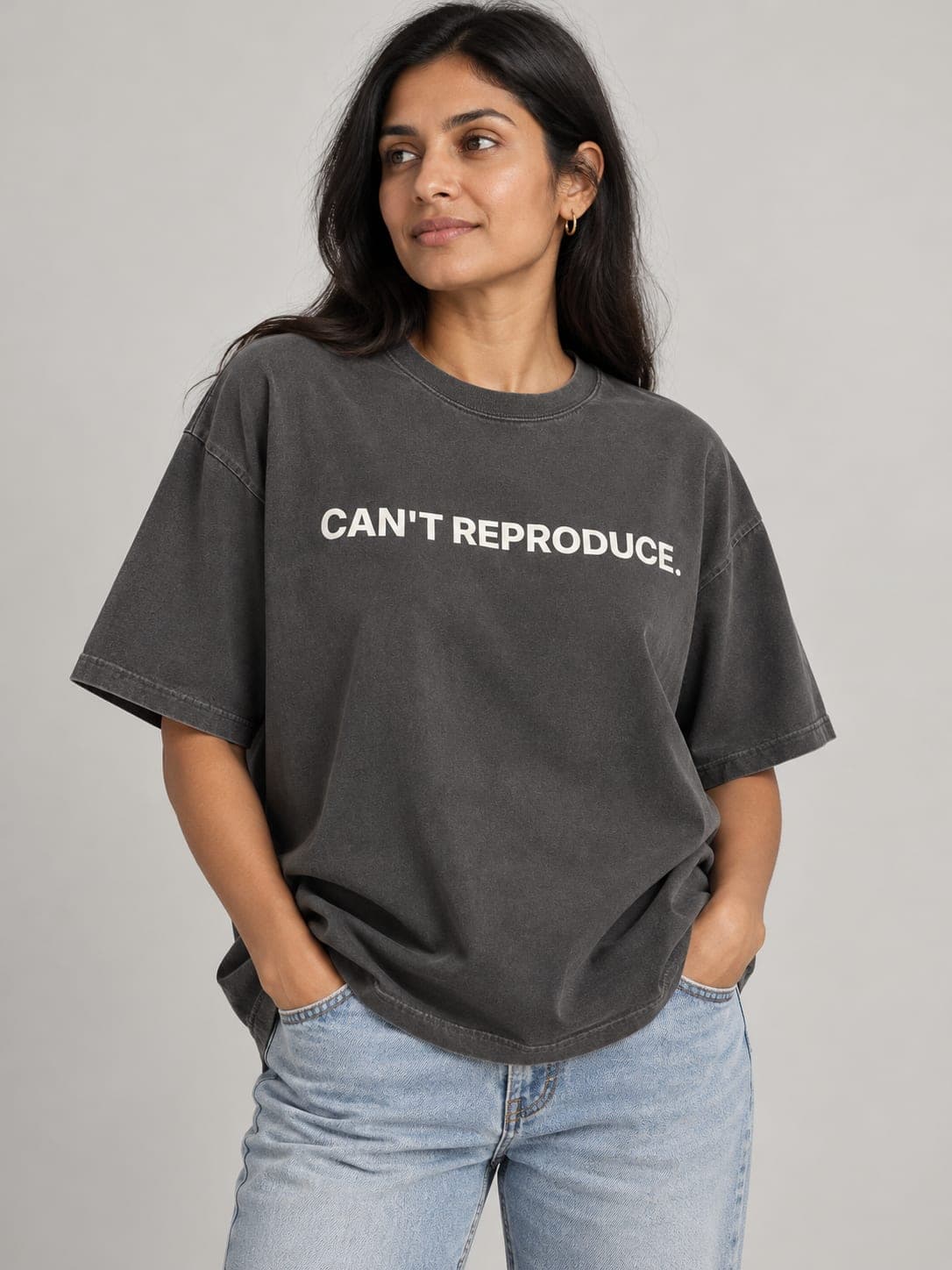 CAN'T REPRODUCE Tee in Faded Coal, worn by a model: CAN'T REPRODUCE. printed center chest. AI-generated mockup.