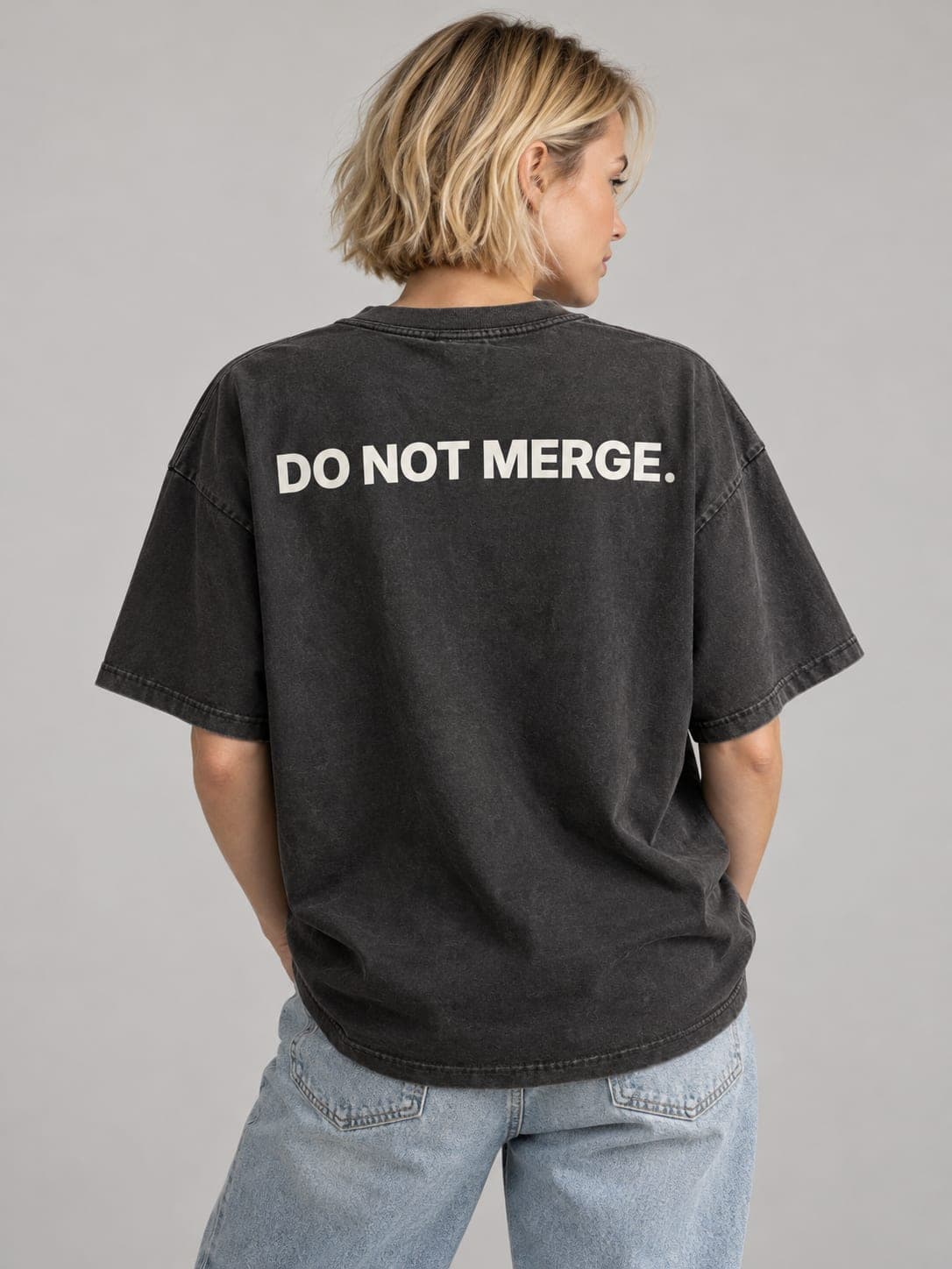 DO NOT MERGE Tee in Faded Black, worn by a model: DO NOT MERGE. printed across the back. AI-generated mockup.
