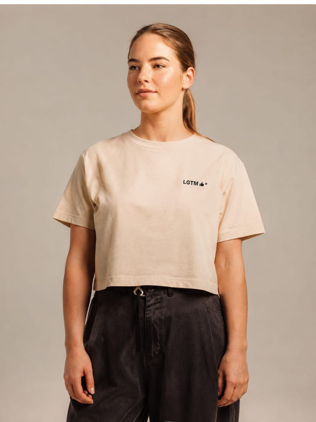 LGTM Crop tee in Bone, worn by a model: LGTM thumbs-up* printed left chest. AI-generated mockup.