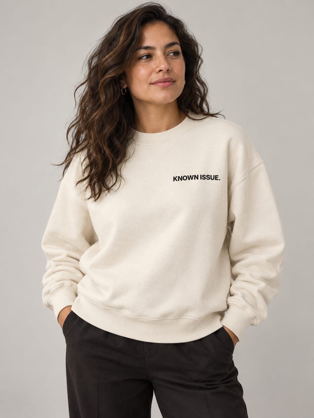 KNOWN ISSUE Crewneck in Faded Bone, worn by a model: KNOWN ISSUE. printed left chest. AI-generated mockup.