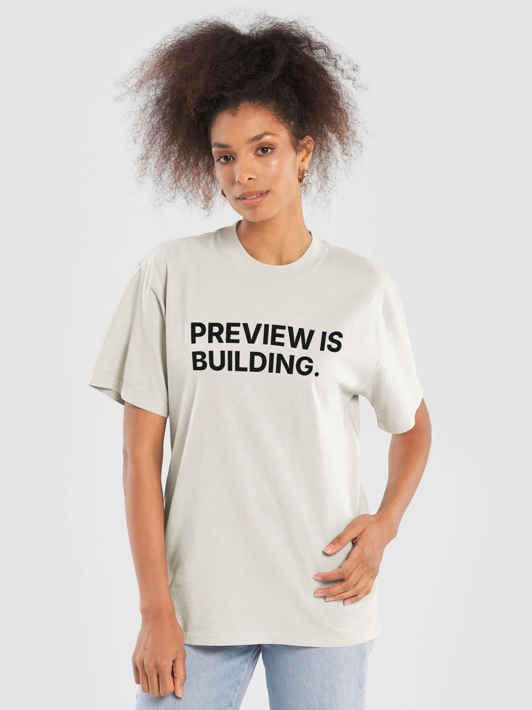 PREVIEW IS BUILDING Tee in Faded Bone, worn by a model: PREVIEW IS BUILDING. printed center chest. Fourthwall product mockup.
